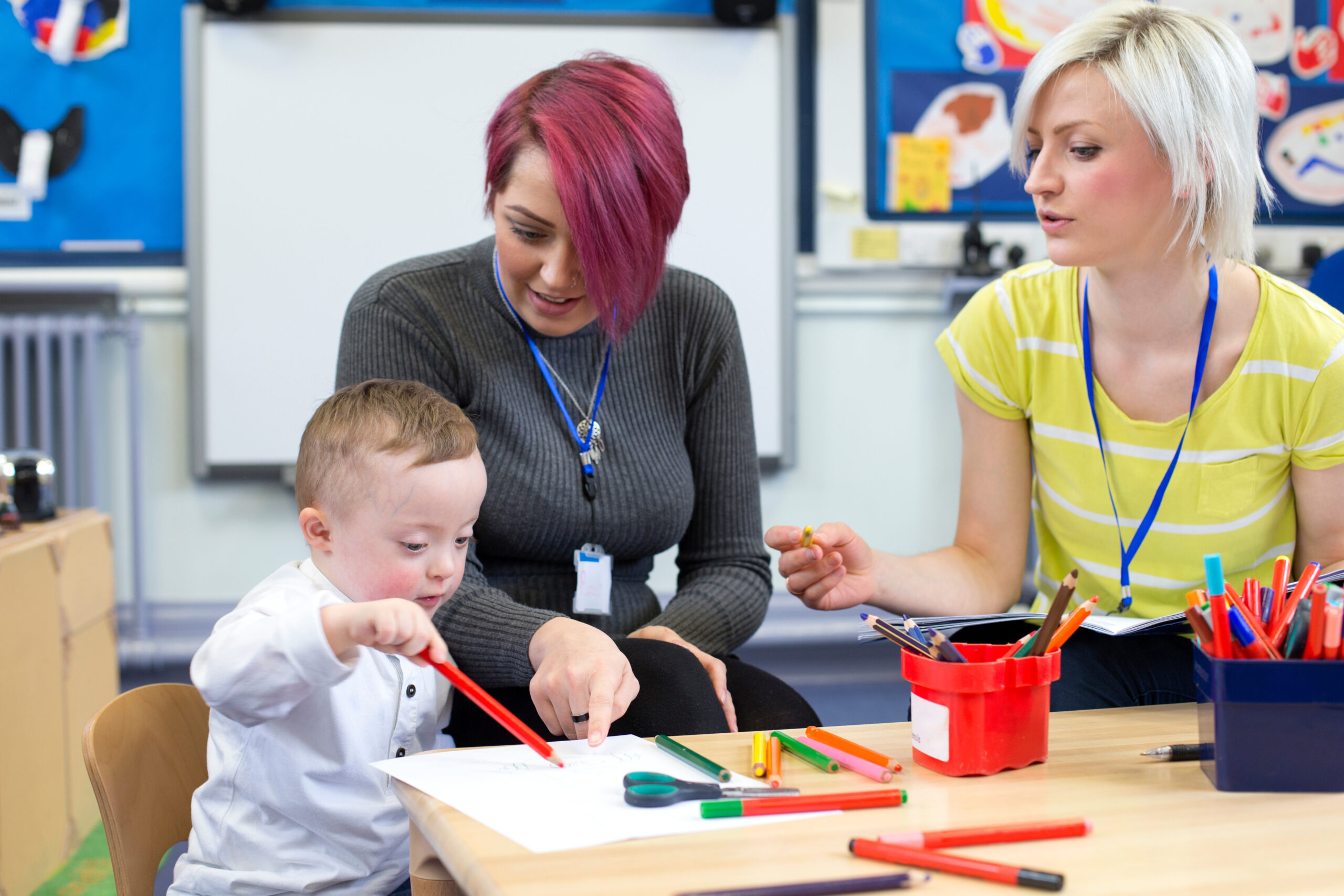 Two teachers and a young child drawing.