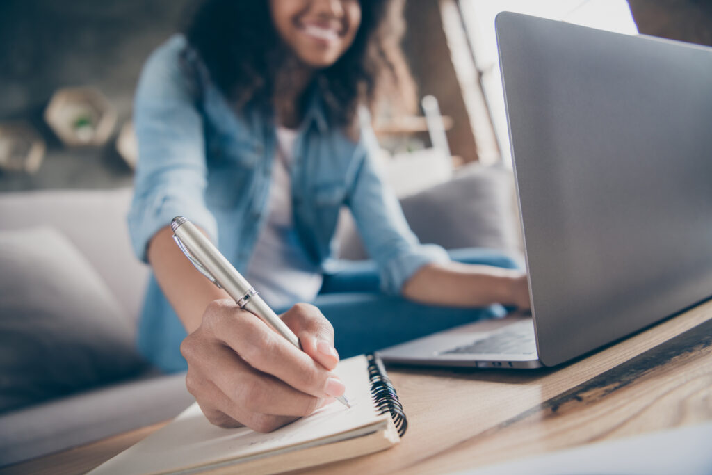 Woman writing on notebook with a laptop.