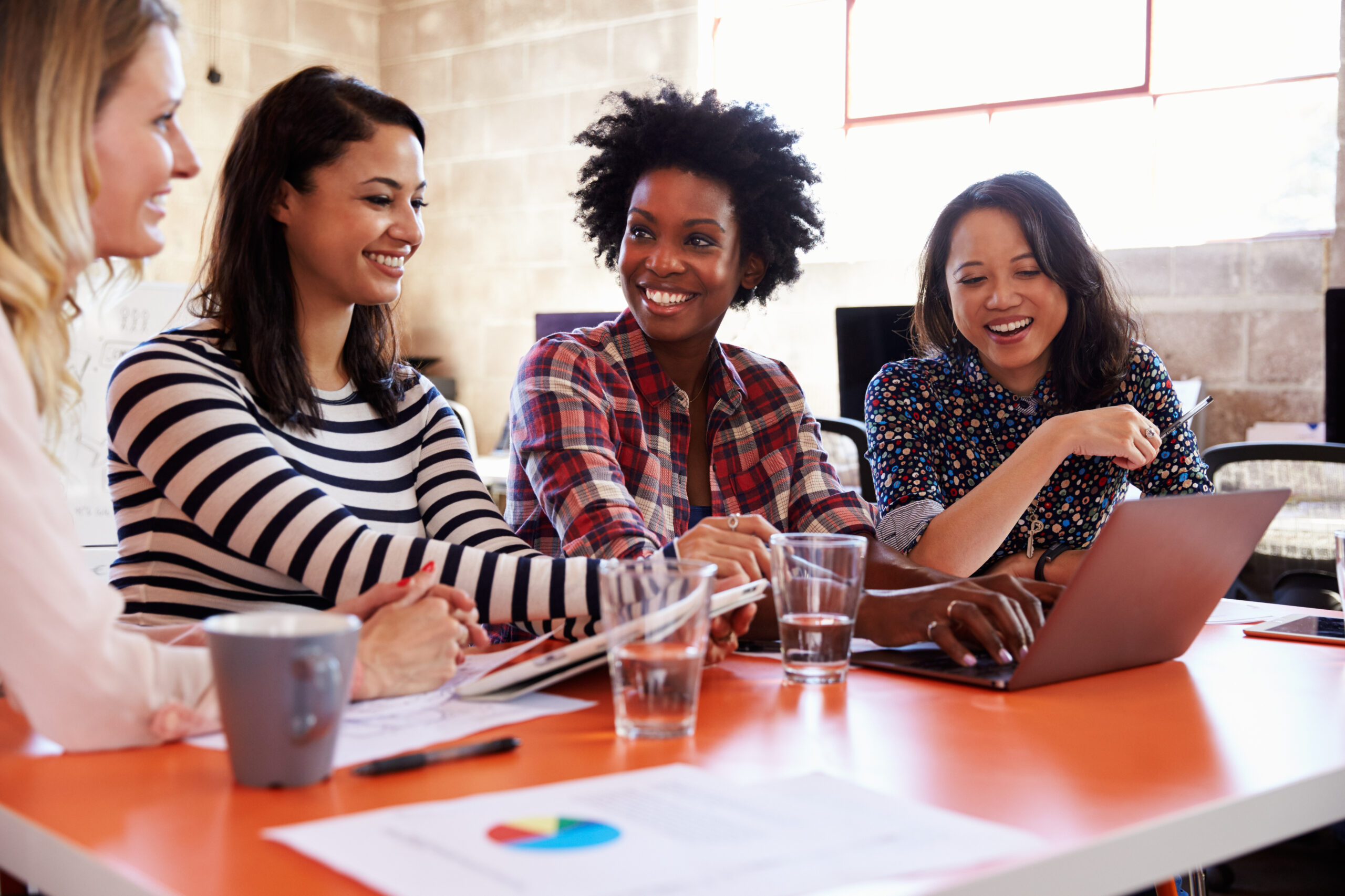 Four women collaborating at a table with a laptop.