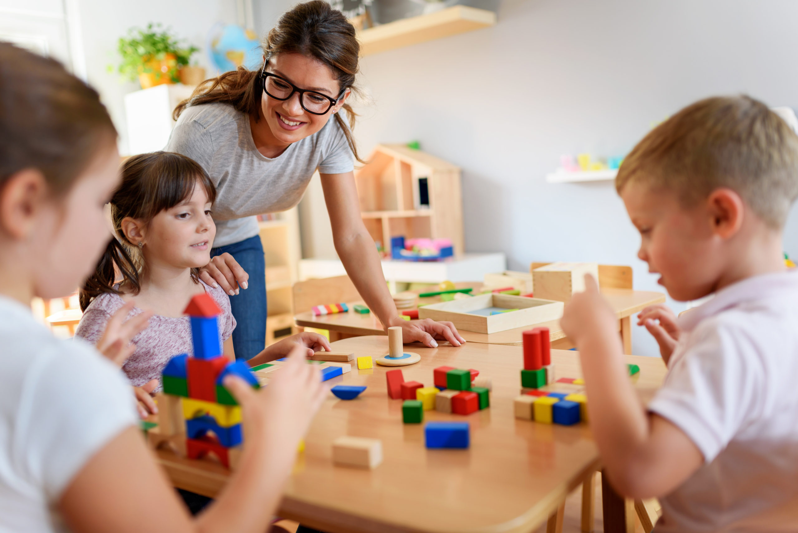 Preschool teacher with children playing with colorful wooden didactic toys at kindergarten