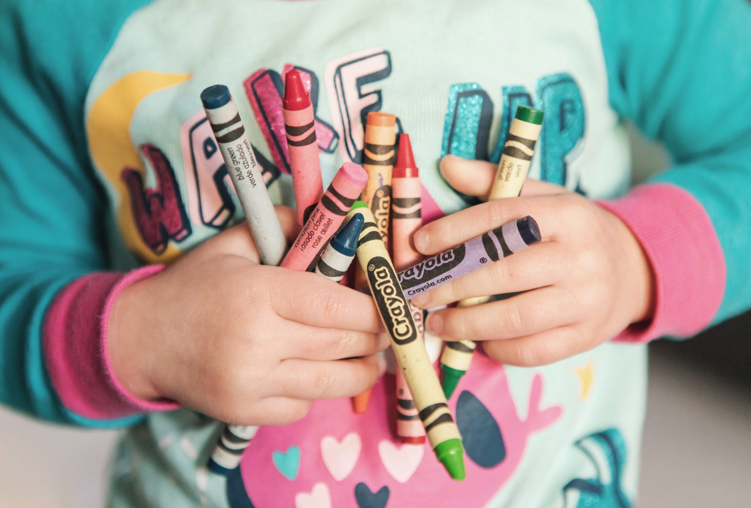 A close up of a childs chest who's holding several crayons