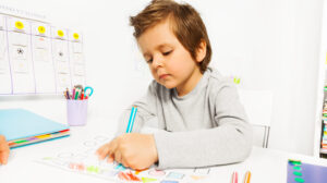 Small boy draws with pencil on the paper during Applied Behavior Analysis ABA sitting at the table indoors