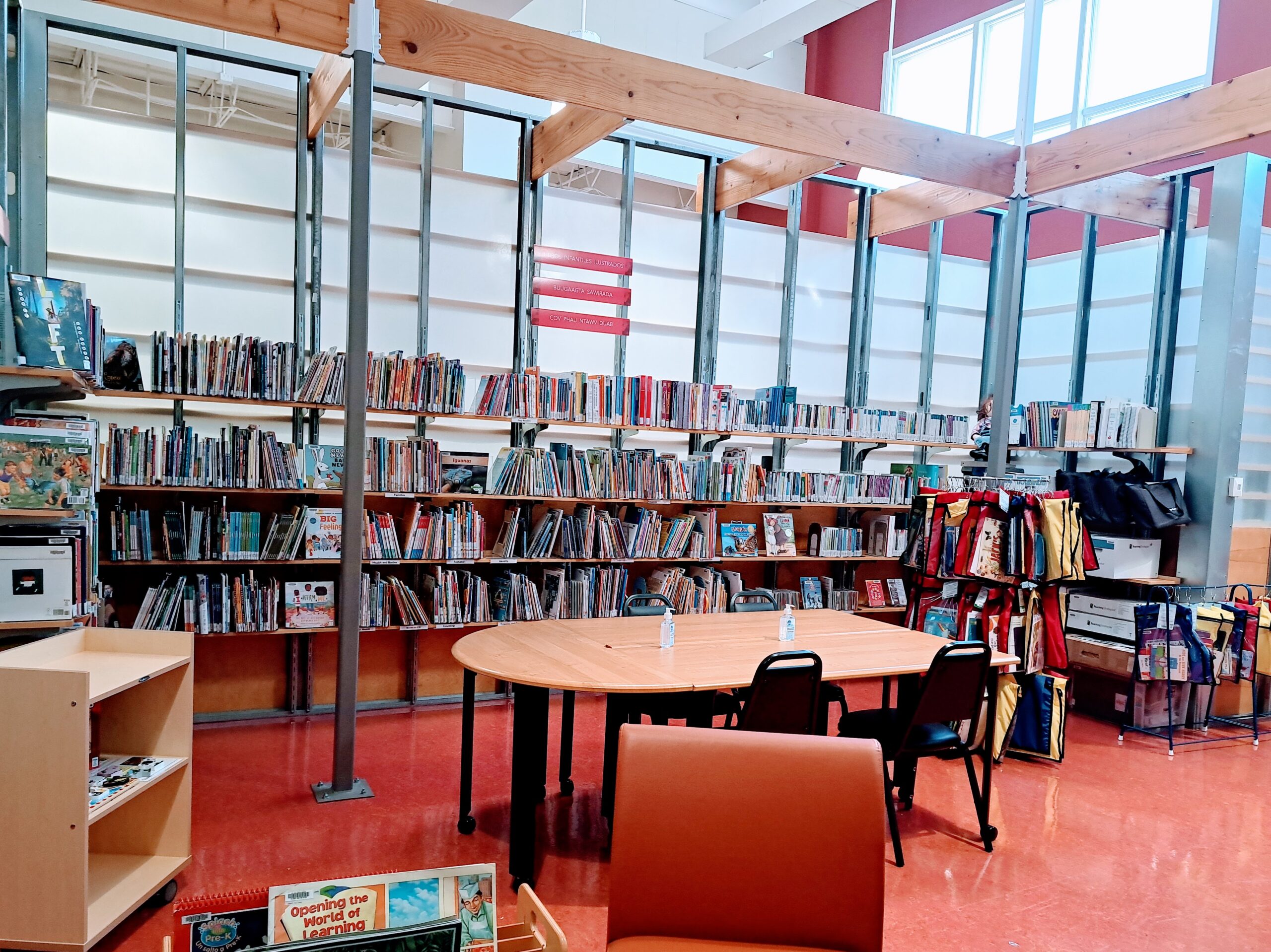 Brightly lit library room with center table surrounded by walls of shelved library books