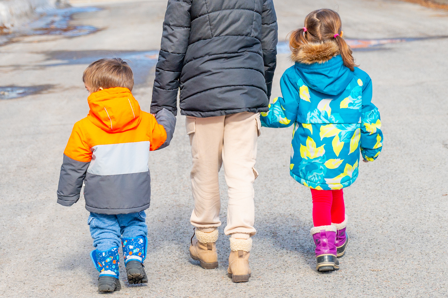 Adult walking in between two small children walking away, in winter coats outside