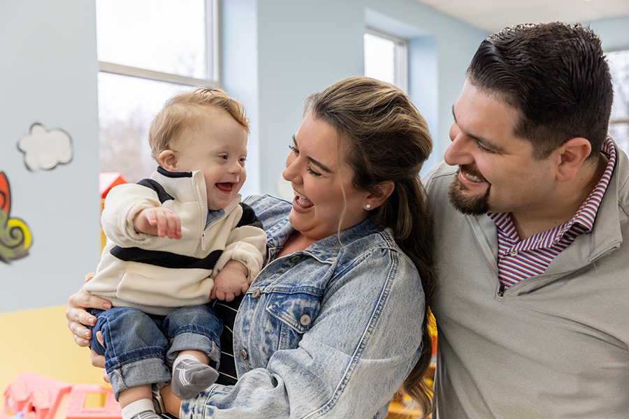 Mother holding toddler who has visible disability with father looking over her shoulder
