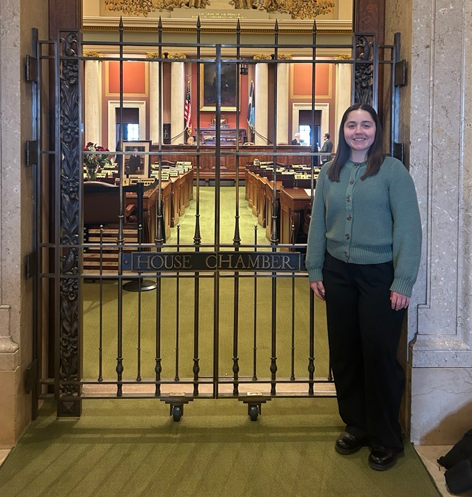 Maddie Wolf standing in front of the House Chamber gate inside the Minnesota Capitol.